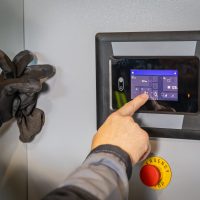 Electrician interacting with touchscreen of modern control panel, managing industrial processes and ensuring safety with emergency stop button